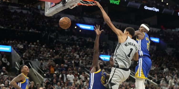 Nov 14, 2025; San Antonio, Texas, USA; San Antonio Spurs forward Victor Wembanyama (1) dunks over Golden State Warriors forward Draymond Green (23) ahead of forward Jimmy Butler (10) and guard Will Richard (3) during the second half at Frost Bank Center. Mandatory Credit: Scott Wachter-Imagn Images