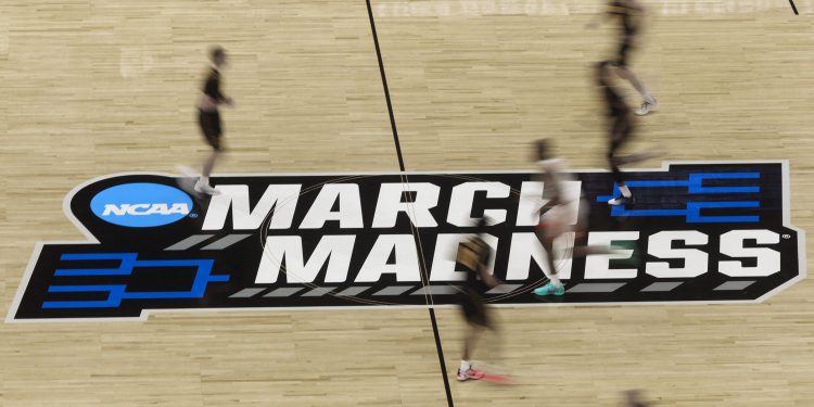 3E32R7W Tampa, Florida, USA. 20th Mar, 2026. The NCAA March Madness logo is visible on the center of the court as players rush by during the first minute of play as the Clemson Tigers take on the Iowa Hawkeyes during the NCAA college basketball tournament at Benchmark International Arena on Friday, March 20, 2026 in Tampa. (Credit Image: © Dirk Shadd/Tampa Bay Times via ZUMA Press Wire)